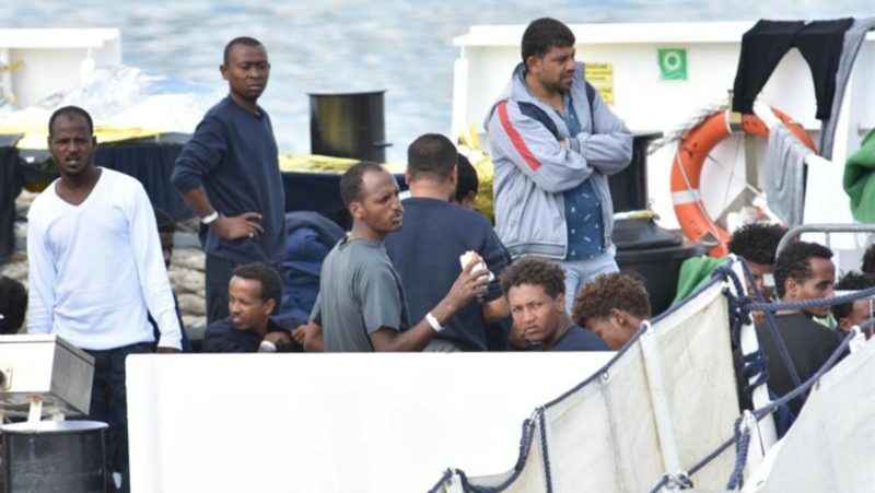 Varios migrantes aguardan a bordo de barco de los guardacostas "Diciotti" en el puerto de Catania