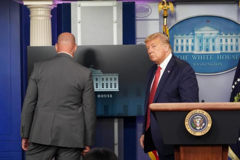 Un agente se dirige a Trump durante la rueda de prensa para comunicarle que deben marcharse tras registrarse un tiroteo cerca de la Casa Blanca.